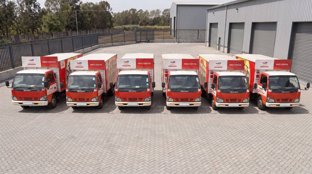 Generated image: a row of red delivery trucks in MKO colours parked side by side in a paved yard.
